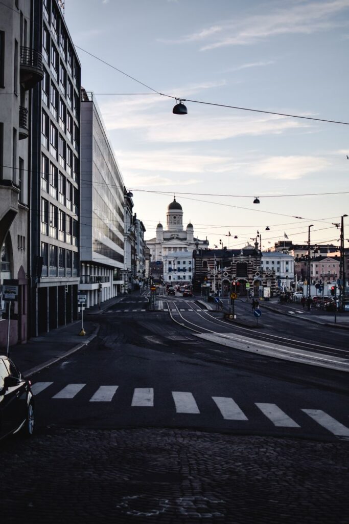 Kuvassa on kaupunkikuva, jossa näkyy leveä katu, suojatie, rakennuksia ja katuvaloja.