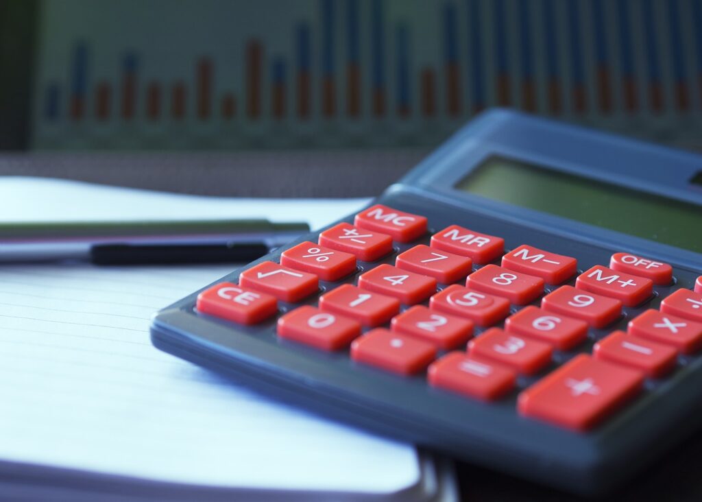 Lähikuva laskimesta, jossa on punaiset numeronäppäimet, lepäämässä avoinna olevan paperin ja kynän päällä, taustalla näkyy...