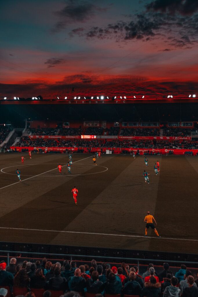 Kuva esittää täytettyä amerikkalaisen jalkapallon stadionia, jossa pelaajat ovat kentällä ja katsomossa on yleisöä iltahämärä
